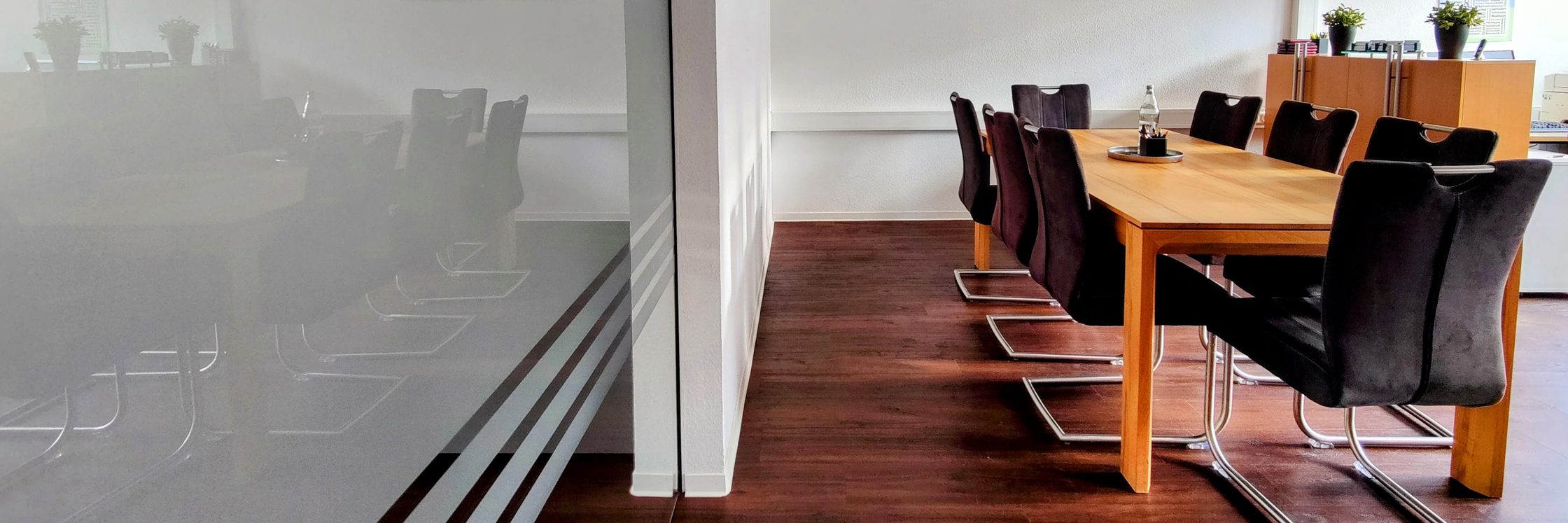 Besprechungsraum in unserem Büro mit Glastür, langem Holztisch und Stühlen